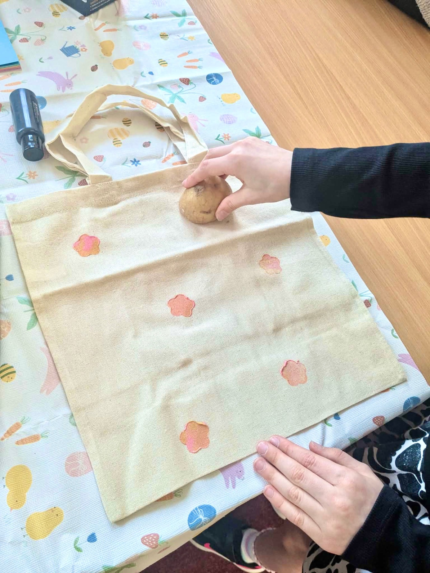 Hands potato printing soft pink flowers onto a cotton tote bag during a craft workshop